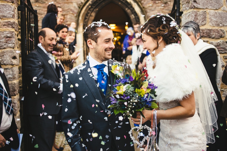 wedding photography at dartmouth church of couple just married being showered with confetti and laughing together