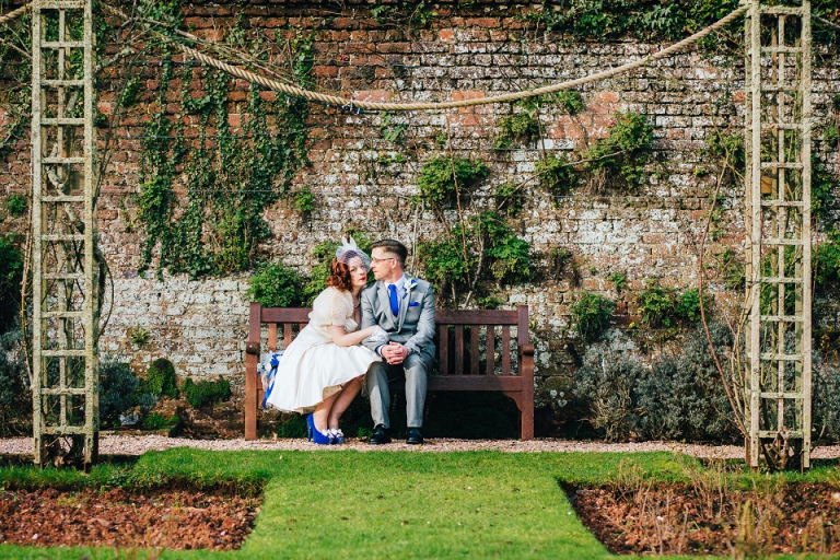eloping couple sitting on bench at cockington court rose garden, modern, star crossed lovers look