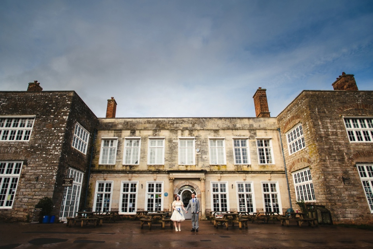 couple alone at their elopement in front of wedding venue cockington court, moody blood skies, wide angle lens