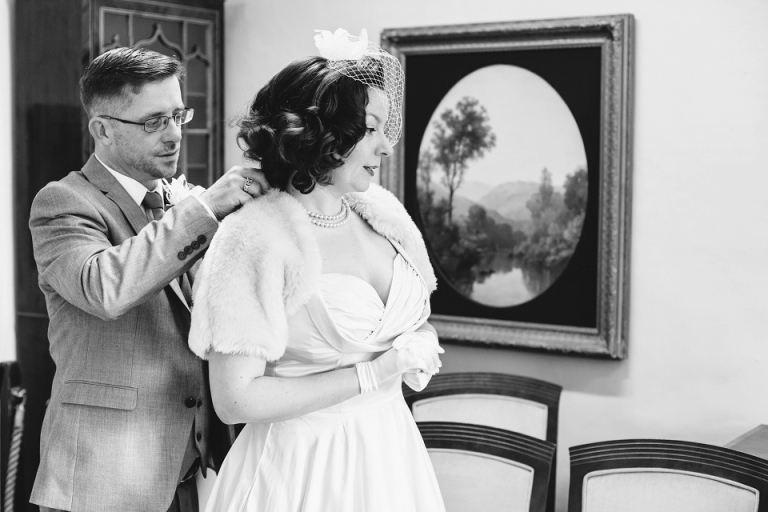 Groom doing up his brides necklace at cockington court registry office before their ceremony