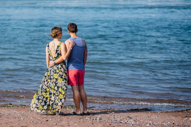 Pre wedding engagement portrait session in Shaldon, Torquay on beach and botanical gardens_ couple with arms around each other looking out to sea